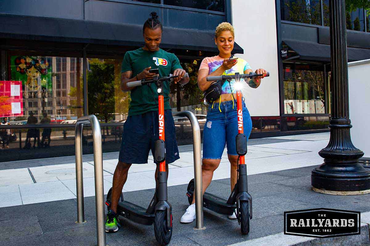 Two young people on ride share scooters in the city.